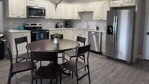A modern kitchen with white cabinetry, stainless steel appliances, and a round dining table with chairs.