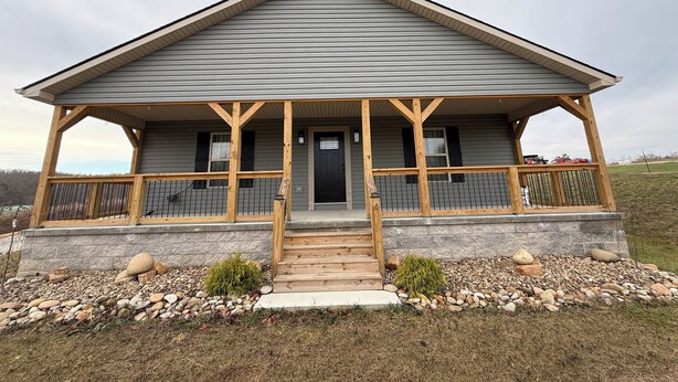 A two-story house with a covered porch, stone foundation, and a view of the surrounding landscape.