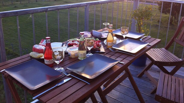 Une terrasse en bois avec une table dressée pour un repas, donnant sur un champ verdoyant.