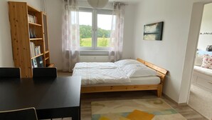 Une chambre avec un lit en bois, un bureau, une bibliothèque et une vue sur la verdure.