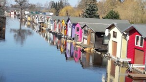 Une rangée de maisons en bois aux couleurs vives longe un cours d’eau paisible.