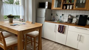 Une cuisine avec une table et des chaises en bois, un réfrigérateur, un four à micro-ondes et des placards sur lesquels est accrochée une serviette.