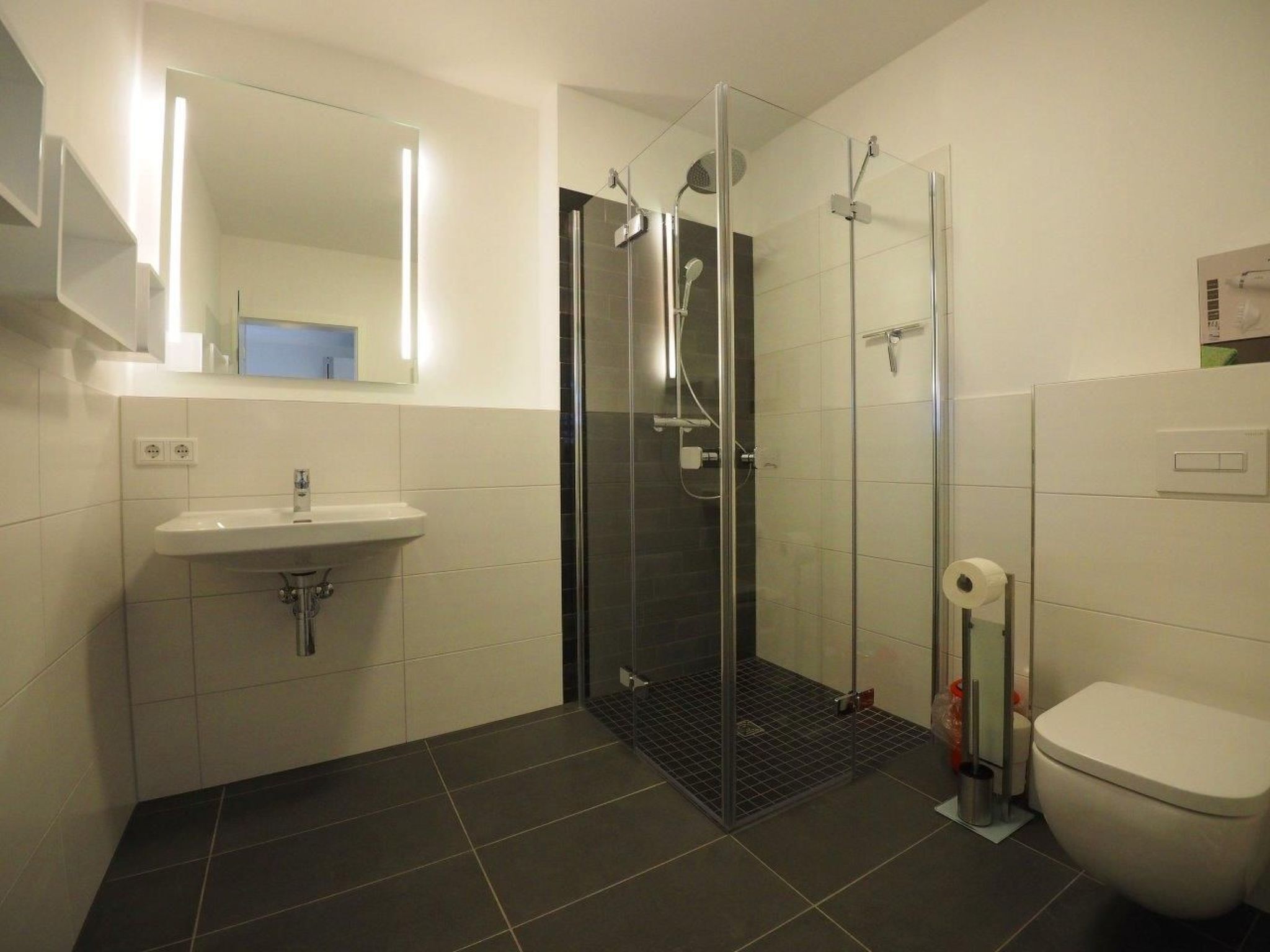 Ein modernes Badezimmer mit Duschkabine aus Glas, einem weißen Waschbecken und einer Toilette.