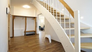 Une pièce spacieuse avec un plancher en bois, un escalier blanc doté de rampes en bois et un petit tabouret blanc près de l’escalier.