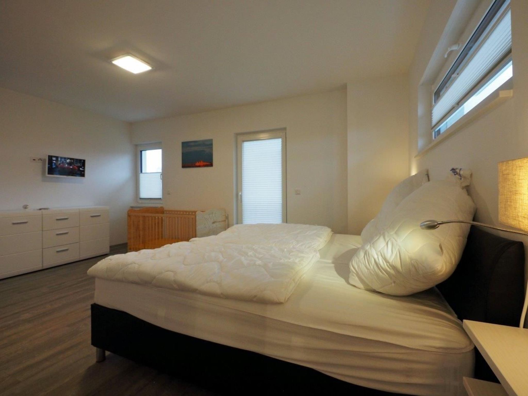 Een slaapkamer met een bed, een dressoir, een radiator, een televisie en een raam met jaloezieën.