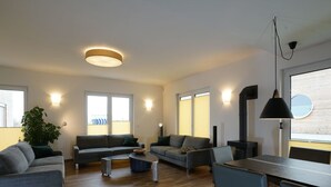 Un salon moderne comprenant un ensemble de canapés, une table basse et un coin repas avec des chaises. On y trouve une grande fenêtre avec des stores, une plante en pot et une cheminée.