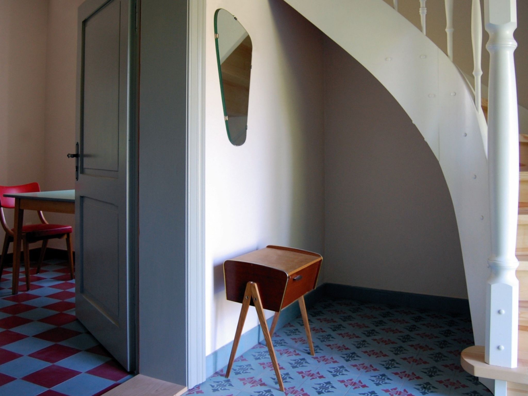 A room with a checkered floor, a desk with a chair, a mirror, and a staircase.