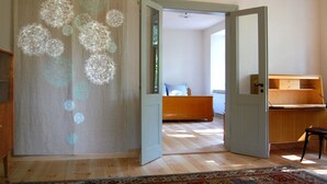 Ein Zimmer mit Holzboden, einem Bett mit blauem Kissen, einem Holzschrank und einer Tür zu einem weiteren Raum.