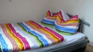 Een bed met een kleurrijke gestreepte deken en kussens, een metalen hoofdbord en een houten nachtkastje met een lamp.