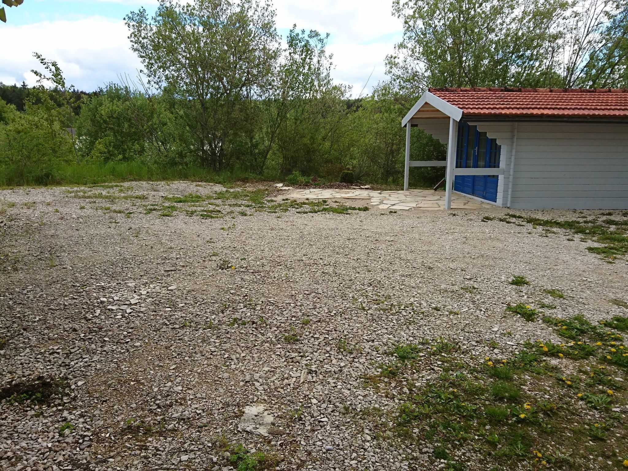 A gravel area with a small building featuring a red-tiled roof and a blue door.