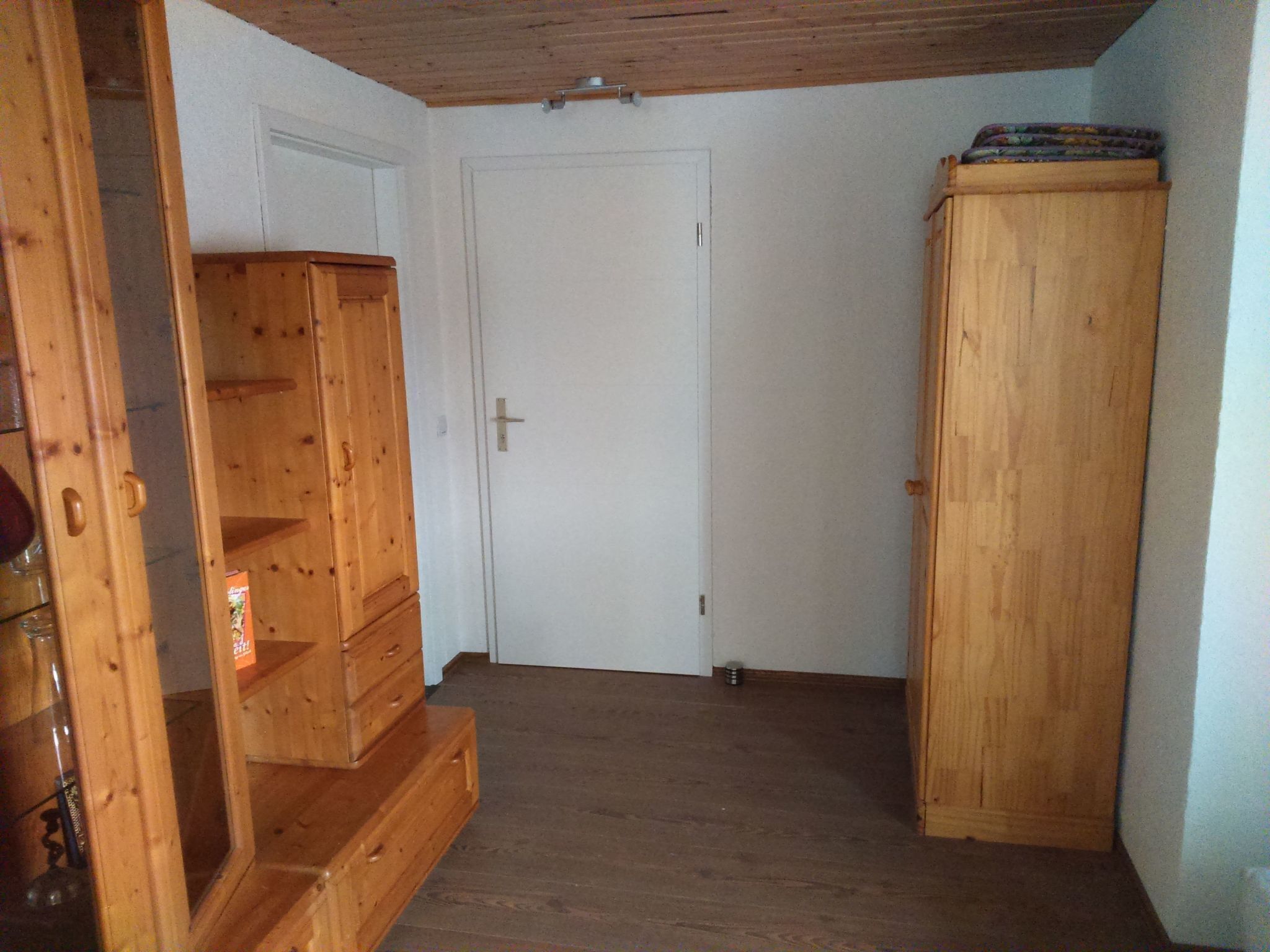 Huone, jossa on puinen portaikko, valkoinen ovi ja puinen kaappi.