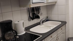 Une cuisine avec des meubles blancs, un four à micro-ondes, une cuisinière, un évier et une machine à café.