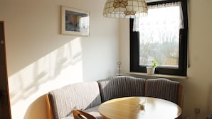Een gezellig eetgedeelte met een ronde houten tafel, een beklede bank met strepen en een decoratieve glazen hanglamp.
