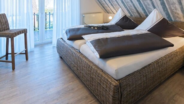 Ein Schlafzimmer mit einem großen Bett, einem Korbstuhl und Blick ins Freie durch eine Schiebetür.