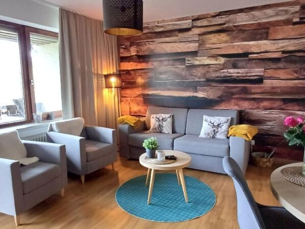 A modern living room with a grey sofa set, a round coffee table, and a wooden accent wall. - Fichtelzauber mit Sauna by Interhome (Mehlmeisel)