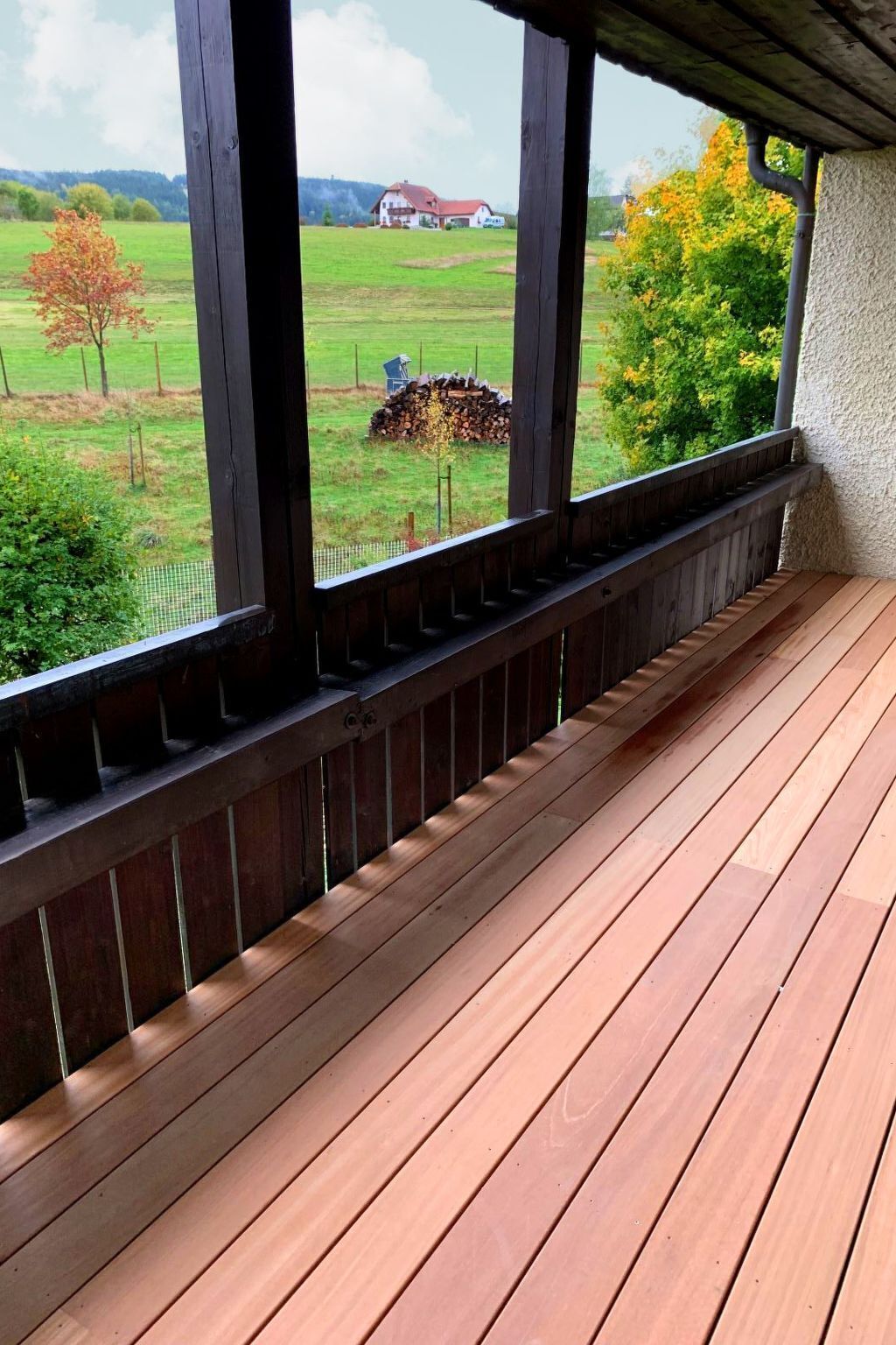 Eine Holzterrasse mit Blick auf eine ländliche Landschaft, einschließlich eines Hauses und Bäumen.