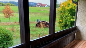Una terraza de madera con vistas a un paisaje rural, que incluye una casa y árboles.