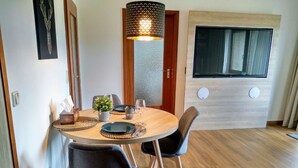 Un comedor con una mesa redonda, dos sillas, una planta en maceta y una lámpara de pared.