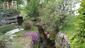 Un estrecho canal de agua con un puente de madera, rodeado de exuberante vegetación y plantas en flor.
