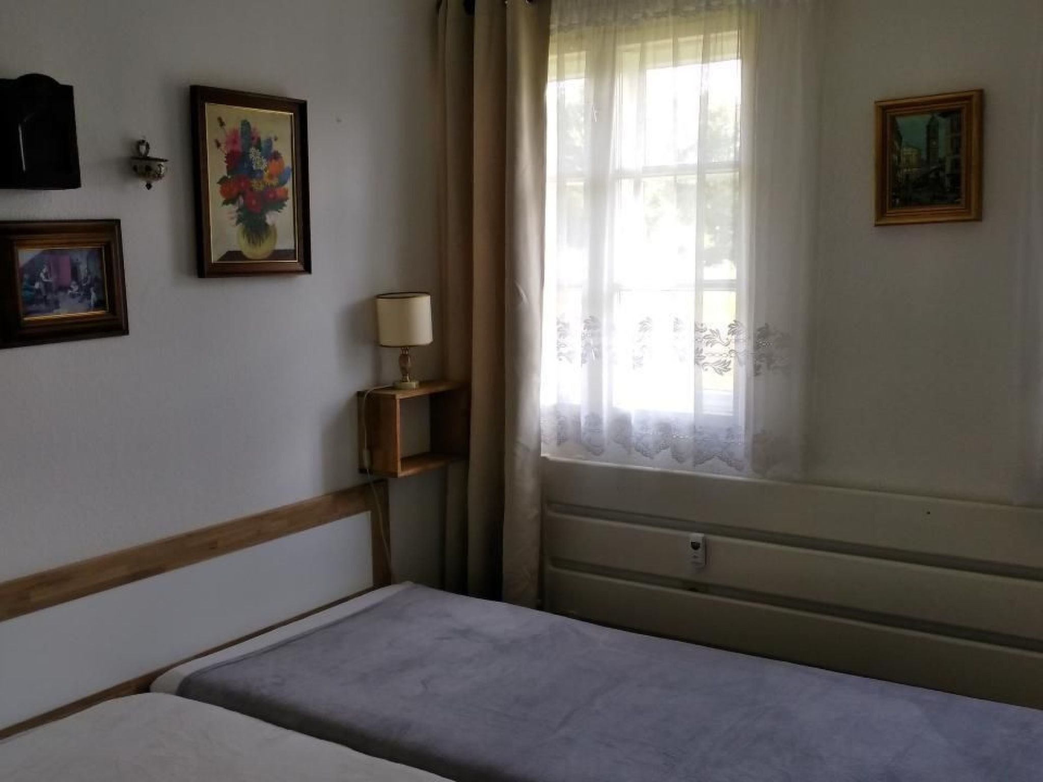 A bedroom with a bed, a bedside table with a lamp, and two framed pictures on the wall.