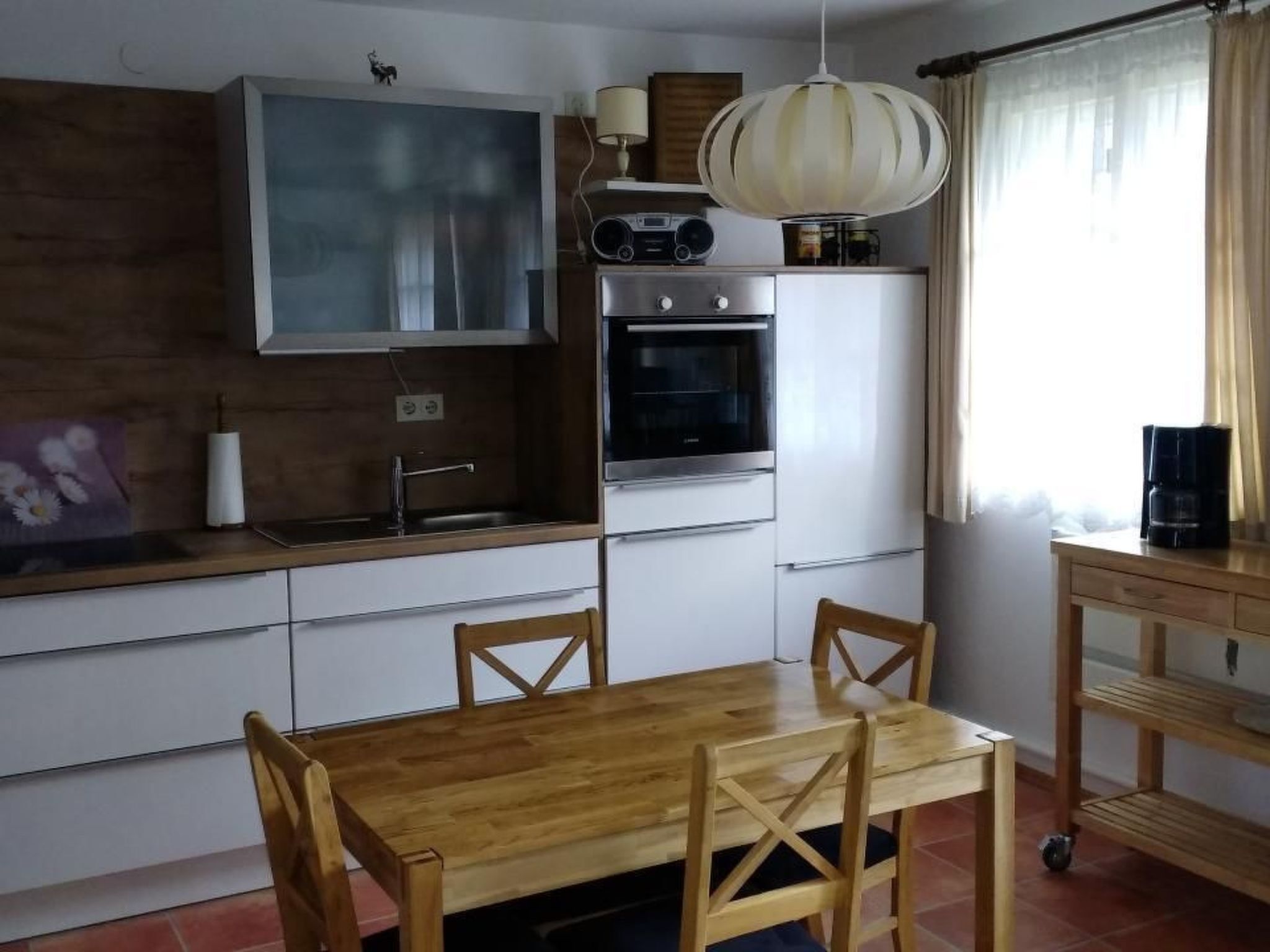 A compact kitchen with a wooden table and chairs, a built-in oven, and a radio above the stove.