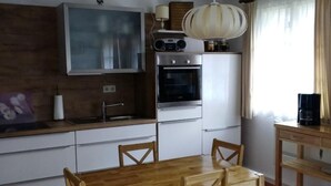 Une cuisine de taille réduite avec une table et des chaises en bois, un four encastré et une radio placée au-dessus de la cuisinière.