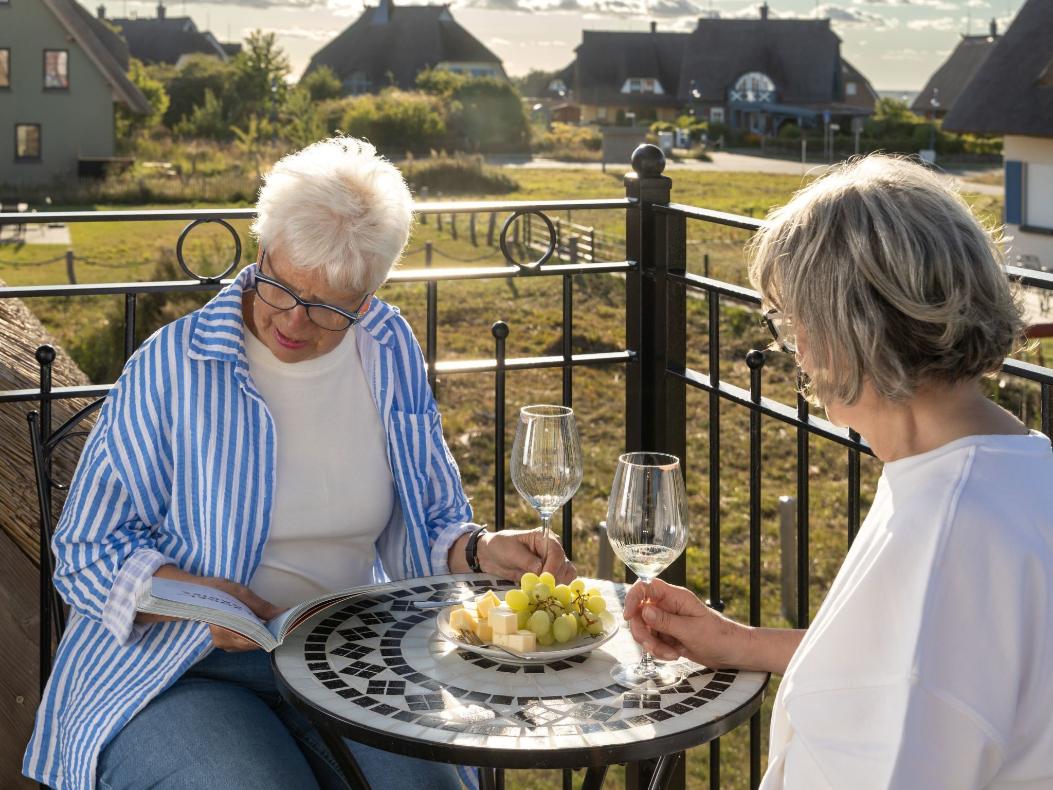 An elderly couple sitting at a table with a book and a plate of cheese and grapes.