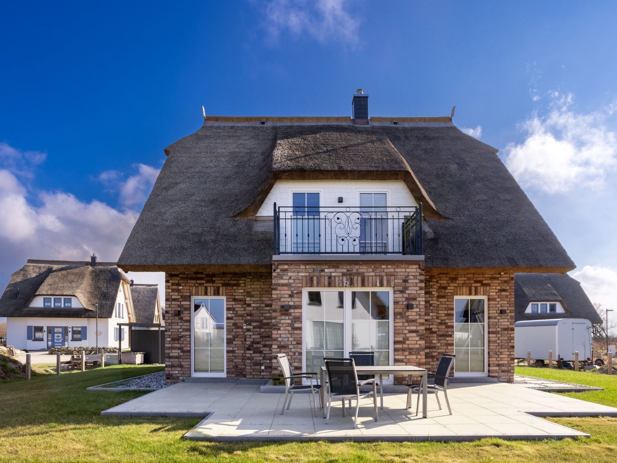 Een woonhuis met twee verdiepingen, rieten dak, bakstenen gevel en een balkon met metalen hekwerk.