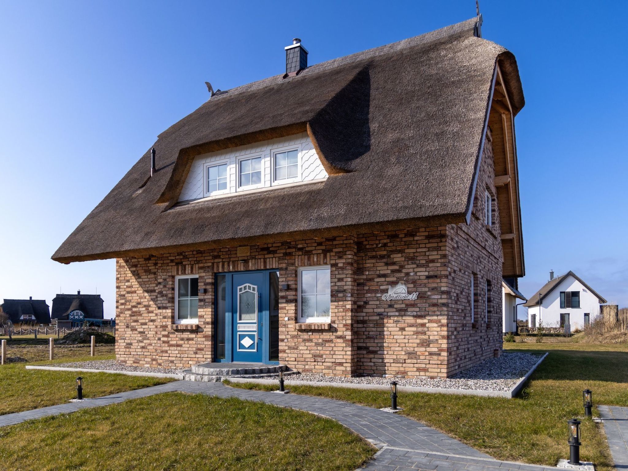 Une maison en briques avec un toit de chaume, une porte bleue et un petit porche à l’avant.