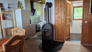 A cozy kitchen with a built-in wood stove, wooden cabinets, and a dining area with a wicker chair. - Tamara in Eppenschlag by Interhome (Eppenschlag)