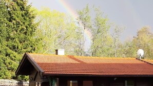 A wooden cabin with a red roof, surrounded by a white picket fence, and a rainbow in the background. - Tamara in Eppenschlag by Interhome (Eppenschlag)