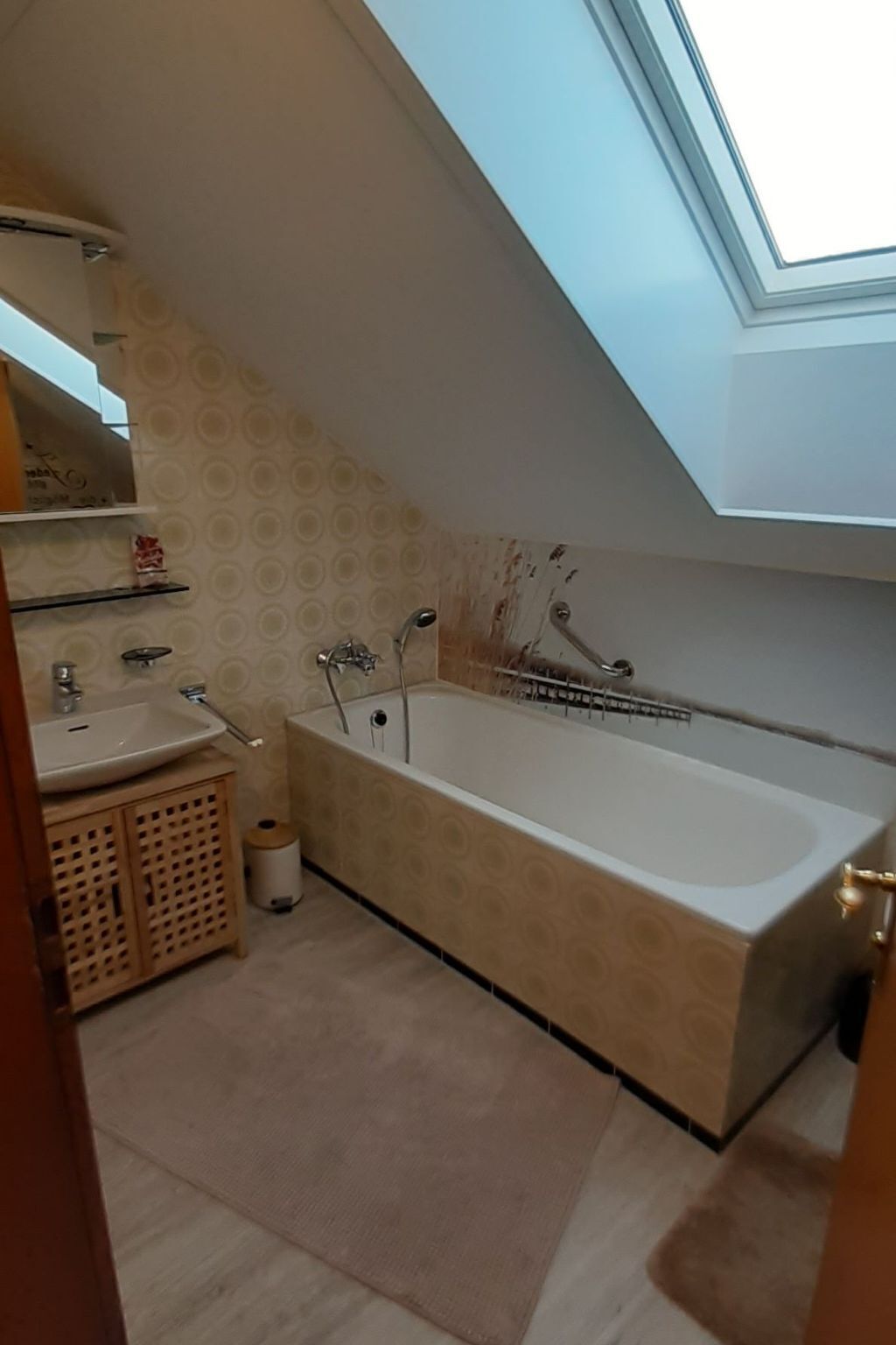 Ein kleines, modernes Badezimmer mit Oberlicht, einer freistehenden Badewanne, einem Waschbecken und einem Holzkorpus.