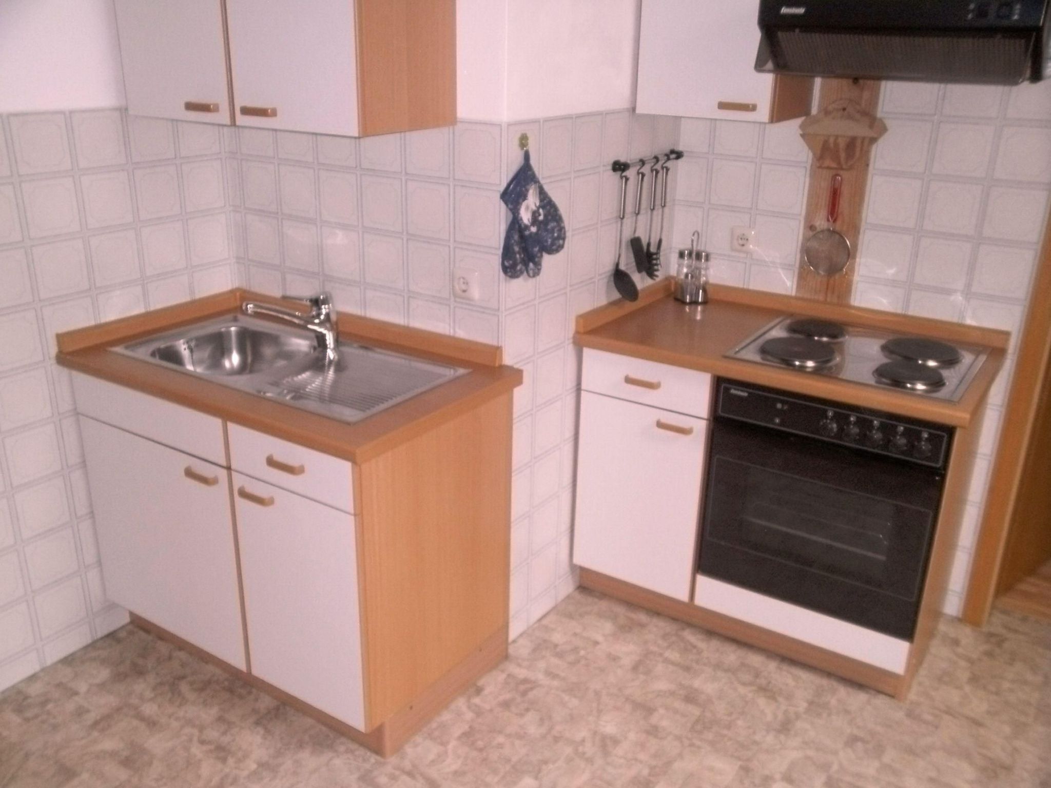 A compact kitchen with white cabinets, a stainless steel sink, a stove, and a dishwasher.