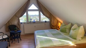 A bedroom with a sloped ceiling, a bed with striped bedding, a chair, a desk, and a window with curtains. - Moderne Wohnung in Karlshagen mit Grill und Garten by Interhome (Karlshagen)
