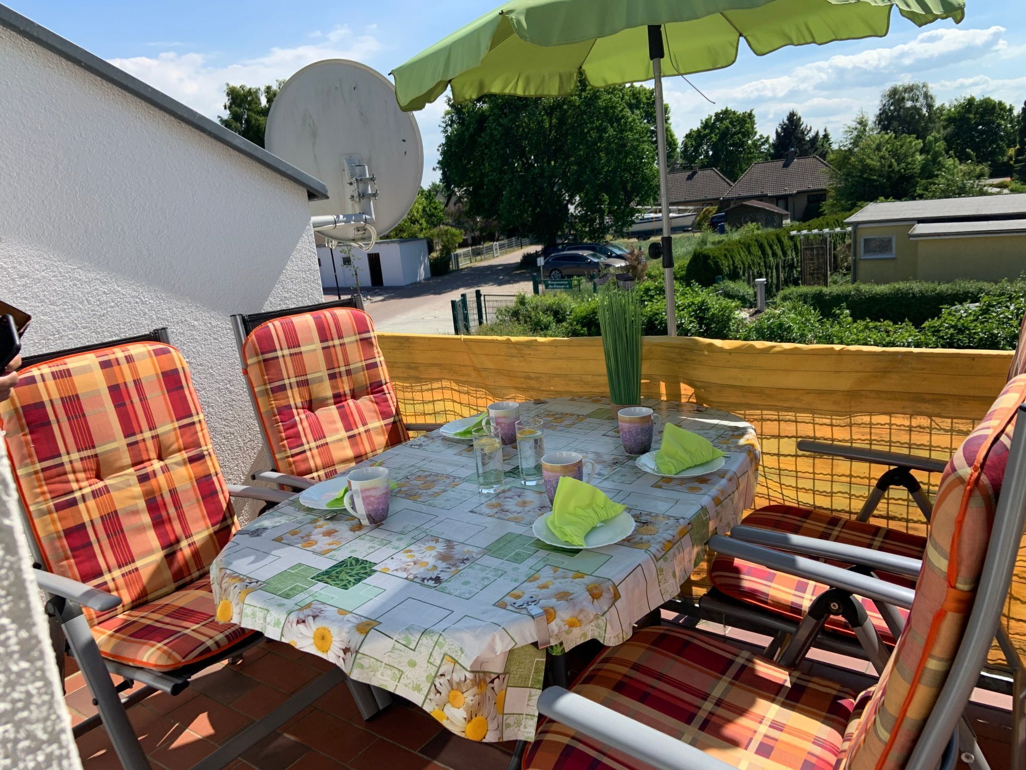 An outdoor patio with a table set for two, surrounded by plaid chairs, under a green umbrella.