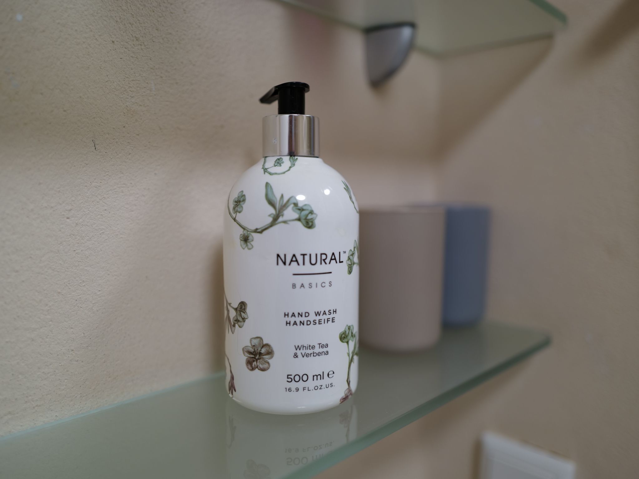 A bottle of hand wash soap on a glass shelf.