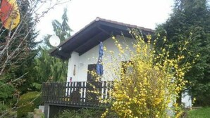 Ein Haus mit Balkon, umgeben von Grün und einem blühenden Baum.