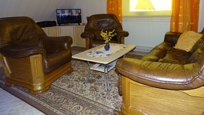 Uma sala de estar com dois sofás de couro, uma mesa de centro com um vaso e uma televisão sobre um móvel.