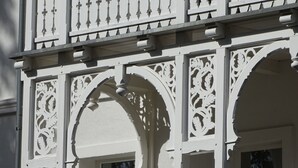 Fachada de edifício com detalhes arquitetônicos brancos e elaborados, incluindo padrões entalhados e janelas em arco.