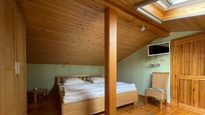 Un dormitorio de madera con techo inclinado, una cama, una mesita, una silla y un armario.