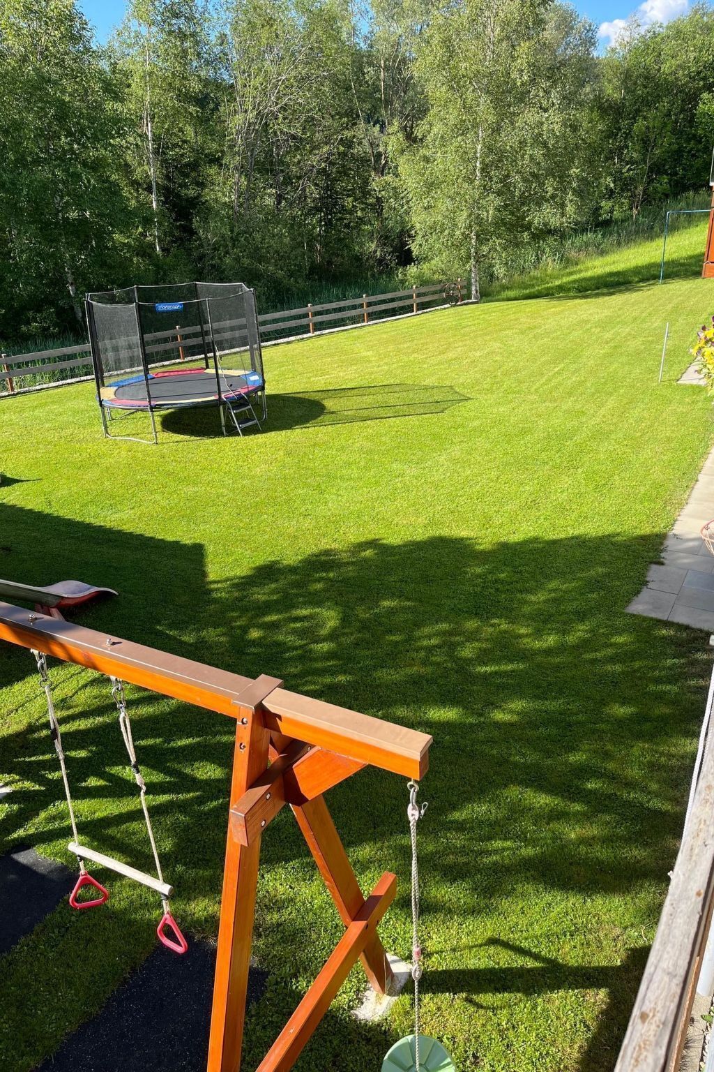 Un patio trasero con un trampolín, un columpio y un banco de madera.