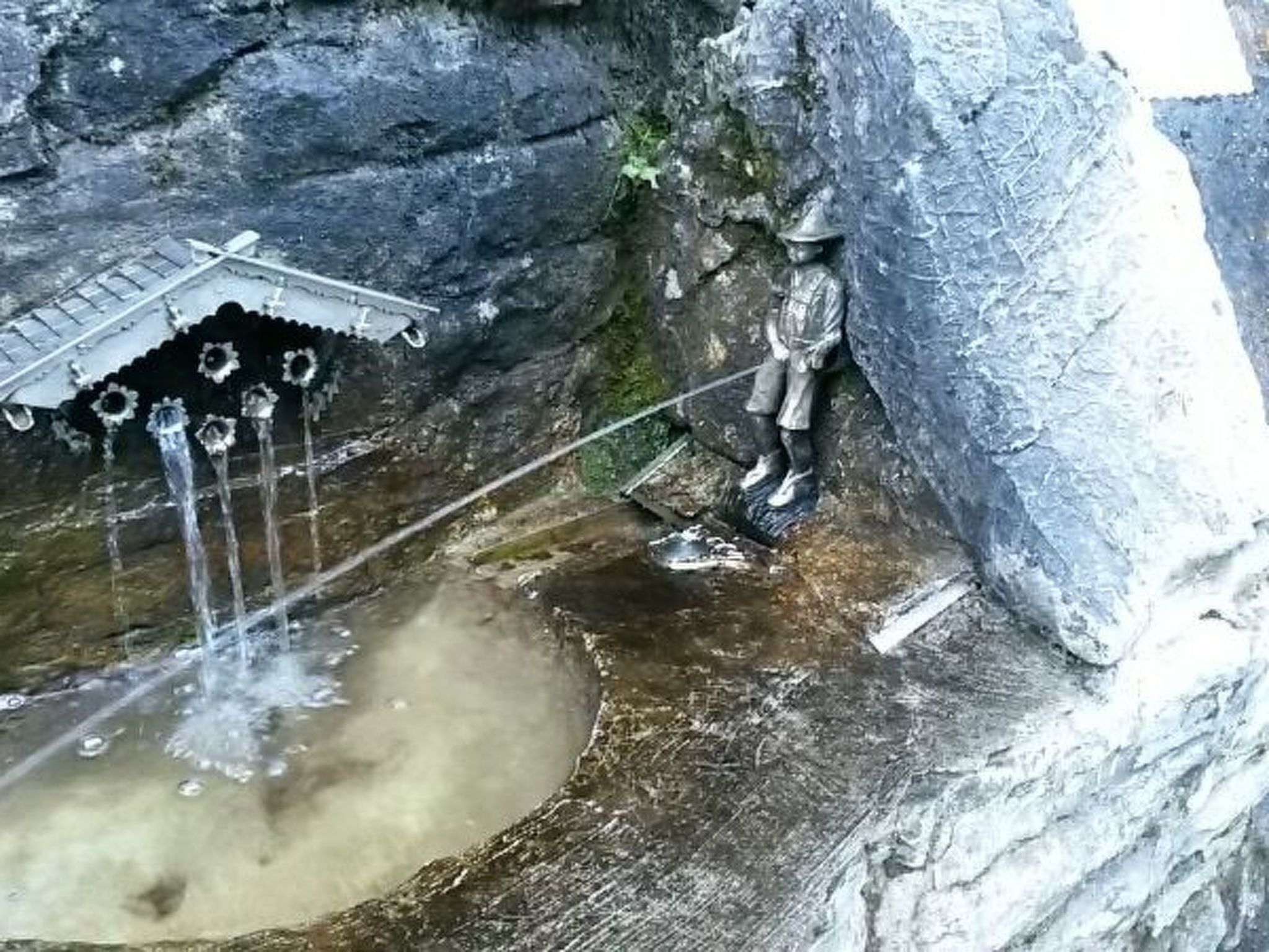 A rock formation with a small waterfall and a statue of a figure in traditional attire.