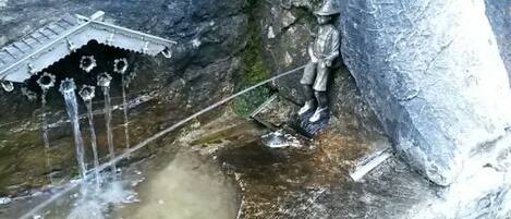 A rock formation with a small waterfall and a statue of a figure in traditional attire.