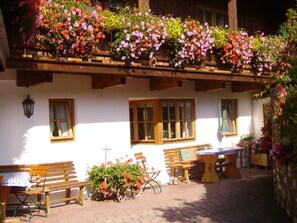 A traditional chalet with a balcony adorned with colorful flowers, wooden benches, and a table with a checkered tablecloth.