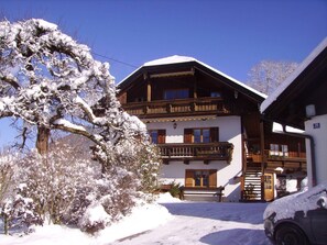 A two-story chalet with a balcony, a wooden staircase, and a car parked in front.