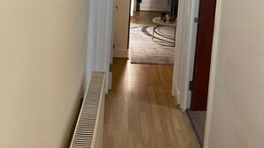 A hallway with a radiator, a door leading to a room with a round table and a rug, and a painting above the door. - Central location, 10 mins away from London Winter Wonderland (London)