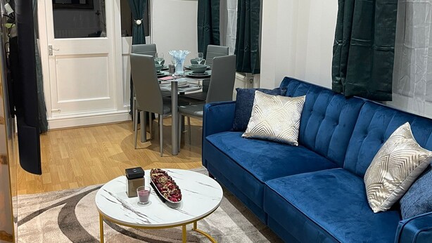 A living room with a blue sofa, a round coffee table, and a dining area with a table and chairs. - Central location, 10 mins away from London Winter Wonderland (London)