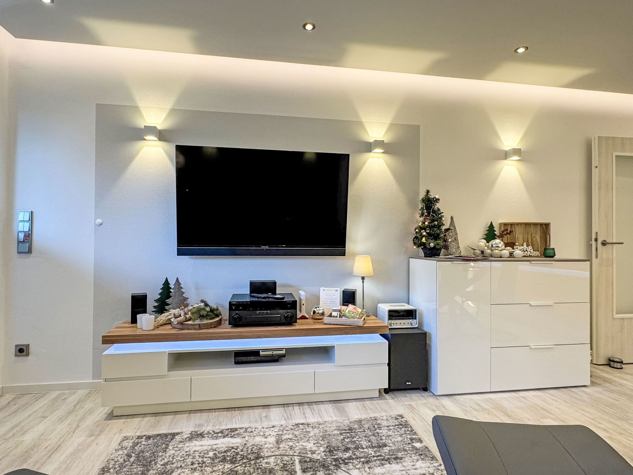 A modern living room with a flat-screen TV, built-in entertainment unit, and a small Christmas tree.