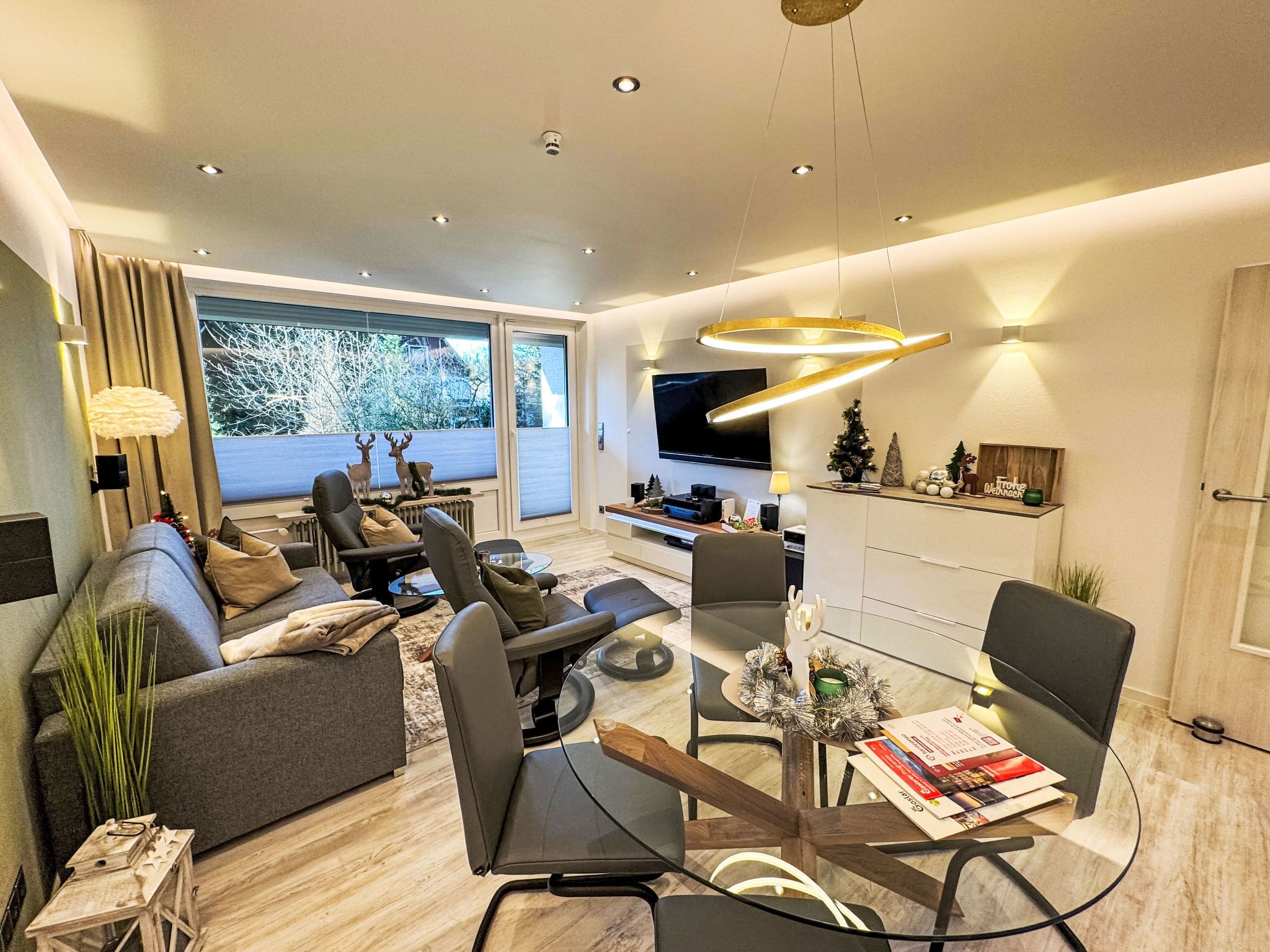 A modern living room with a sofa, chairs, a glass coffee table, and a TV.