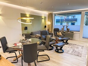 Ein modernes Wohnzimmer mit einem runden Glastisch, Ledersofas und einem großen Fenster mit Blick auf ein Gebäude.